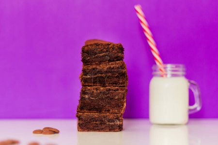 Foto de Brownie y vaso de leche sobre fondo morado. Composición de estilo de comida moderna - Imagen libre de derechos