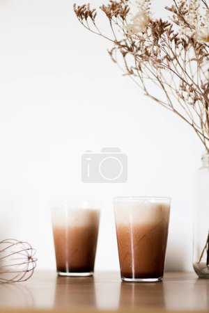 Foto de Dos vasos de café dalgona con leche y flores secas sobre mesa de madera. - Imagen libre de derechos