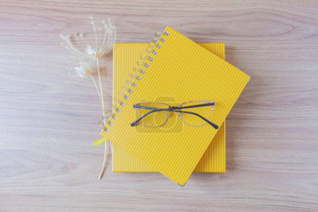 Photo for Yellow planners with glasses on the top and wild flowers aside on wooden table. home office desk workspace - Royalty Free Image