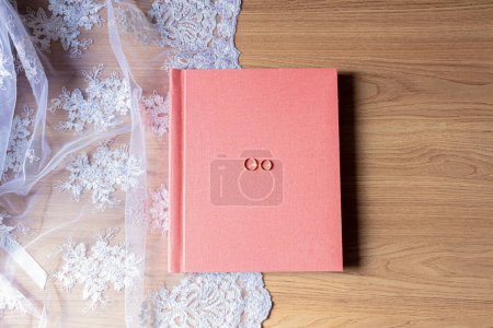 Foto de Álbum de fotos rosa con anillos de boda en tela blanca y mesa de madera - Imagen libre de derechos