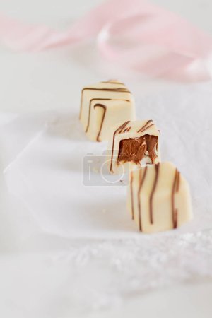 Photo for Delicious white chocolate candies and pale pink ribbon on white background. - Royalty Free Image