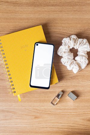 Photo for Female home office desk workspace with scrunchie, planner and mobile phone on wooden table. - Royalty Free Image