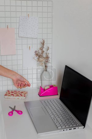 Téléchargez les photos : Esthétique minimaliste bureau à domicile espace de travail Main féminine en utilisant du ruban adhésif près d'un ordinateur portable sur un bureau blanc. - en image libre de droit