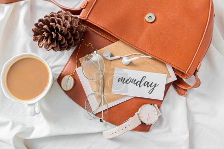 Photo for Fashion composition with female accessories and stationary on messy bed background. Bag with craft envelopes, earphones, glasses, necklace, wrist watch and card with phrase Monday. Flat lay, top view. Autumn, fall concept. - Royalty Free Image