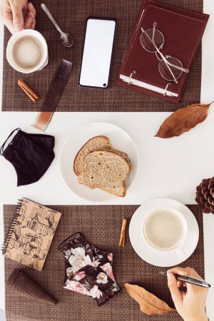 Foto de Vista superior de una pareja, o compañeros de trabajo tomando el desayuno con café y máscara en la mesa blanca - Imagen libre de derechos