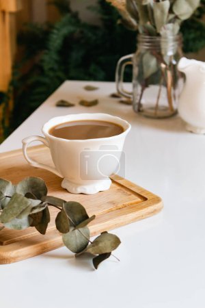 Foto de Taza de café con hojas de eucalipto sobre tabla de madera - Imagen libre de derechos