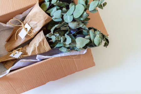 Téléchargez les photos : Bouquets d'eucalyptus vert en boîte artisanale sur blanc. Concept de boutique de fleurs. - en image libre de droit