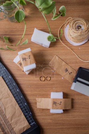 Foto de Recuerdos de boda de bricolaje: jabón de coco, anillos de boda dorados, cortador de papel, sello en una mesa de madera - Imagen libre de derechos