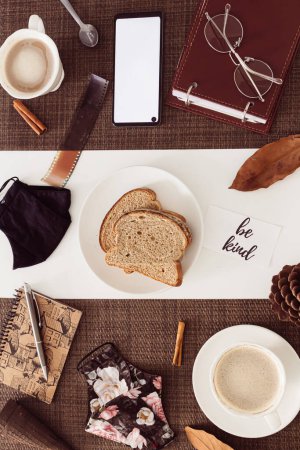Foto de Composición de desayuno de otoño con café, mascarilla, pan en rodajas y hojas secas alrededor en mesa blanca - Imagen libre de derechos