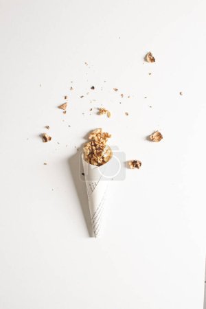 Photo for Top view of walnut kernels in paper cone with walnut shells around on white background. Cosy autumn aesthetic composition - Royalty Free Image