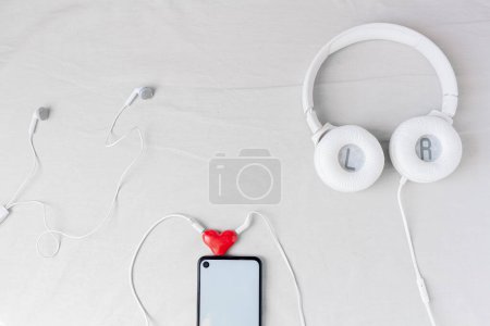 Téléchargez les photos : Modélisation de bureau à domicile avec smartphone, diviseur audio en forme de coeur et écouteurs sur fond blanc. - en image libre de droit