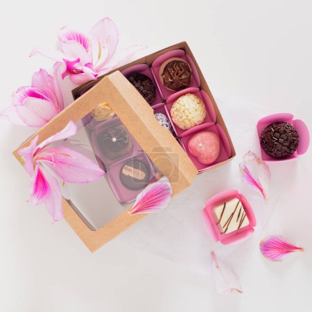 Téléchargez les photos : Boîte cadeau de bonbons décorés avec des fleurs sur fond blanc. Composition printemps féminine. Stylisme alimentaire. - en image libre de droit