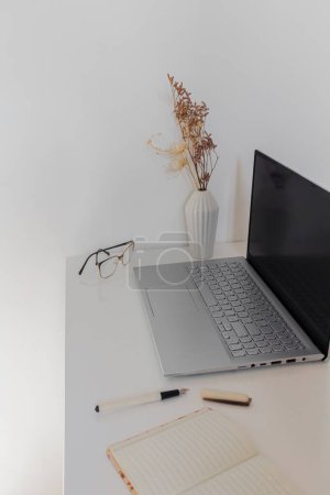Foto de Espacio de trabajo del escritorio de la oficina en el escritorio blanco con el ordenador portátil, el cuaderno y las gafas - Imagen libre de derechos