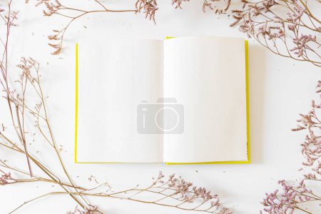 Foto de Marco redondo hecho de flores lila sobre fondo blanco con bloc de notas en blanco abierto. Piso tendido, vista superior. - Imagen libre de derechos