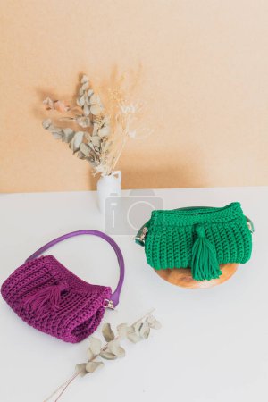 Téléchargez les photos : Vue rapprochée de sacs à main colorés au crochet avec des fleurs séchées sur fond beige. Concept de mode - en image libre de droit