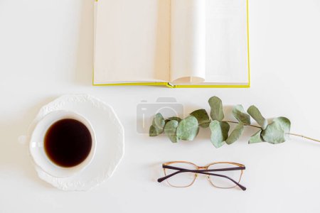Téléchargez les photos : Vue du dessus de tasse de café avec branche d'eucalyptus, verres et livre sur fond blanc - en image libre de droit
