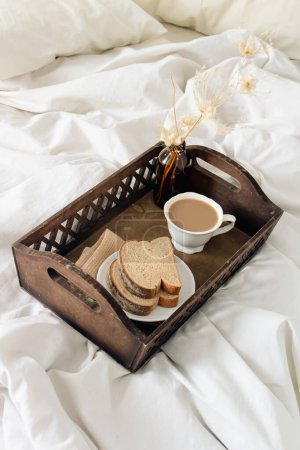 Téléchargez les photos : Petit déjeuner sur plateau vintage en bois foncé au lit avec drap beige clair et oreillers. concept matin romantique. - en image libre de droit