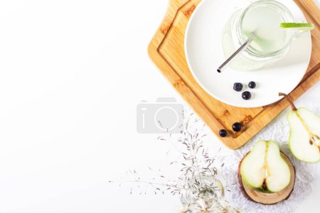 Photo for Aesthetic minimalist composition. Glass with green lemonade, pear halves and blueberries on white background. Summer cold drink concept. - Royalty Free Image