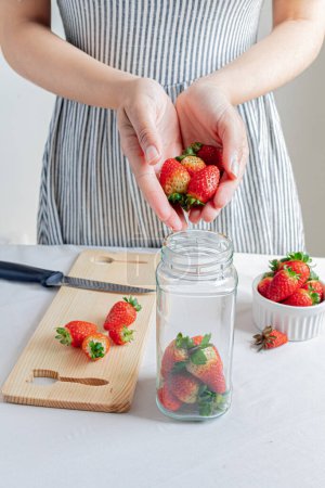 Photo for Young woman put strawberries on a jar. Organic food storage concept. - Royalty Free Image
