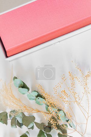 Téléchargez les photos : Album photo rose avec fleurs séchées et feuilles d'eucalyptus sur drap de lit blanc - en image libre de droit