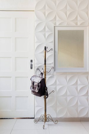 Foto de Salón clásico moderno en colores blancos con mochila borgoña colgada en perchero. Concepto minimalista de decoración para el hogar. - Imagen libre de derechos
