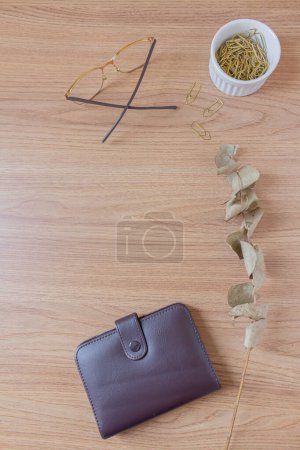 Foto de Área de trabajo minimalista de escritorio de oficina con gafas, billetera, rama de eucalipto seco, clips de papel dorados sobre un fondo de madera. Asiento plano, vista superior. Concepto de finanzas. - Imagen libre de derechos