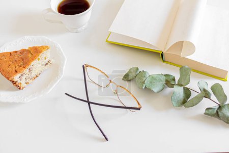 Foto de Composición del desayuno con café, libro, pedazo de pastel y vasos sobre fondo blanco. Concepto de rutina matutina lenta. - Imagen libre de derechos