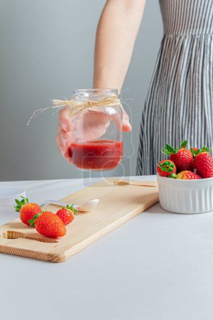 Photo for Young female hand holding a jar of strawberry marmalade. - Royalty Free Image