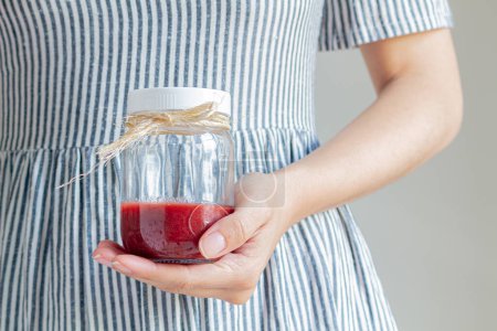 Photo for Young female hand holding a jar of strawberry marmalade. - Royalty Free Image