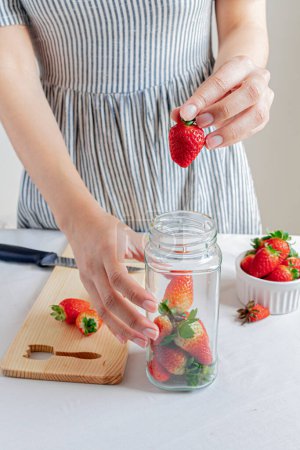 Téléchargez les photos : Une jeune femme a mis des fraises sur un pot. Concept de stockage des aliments biologiques. - en image libre de droit