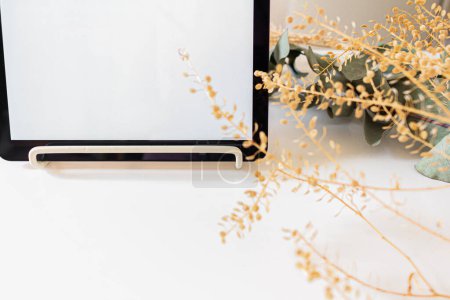 Foto de Vista superior de la tableta digital decorada con flores secas sobre fondo blanco - Imagen libre de derechos