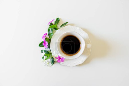 Foto de Taza de café negro, flores pequeñas de color rosa y púrpura y hojas de mora sobre fondo blanco. Piso tendido, vista superior. Concepto primavera. - Imagen libre de derechos