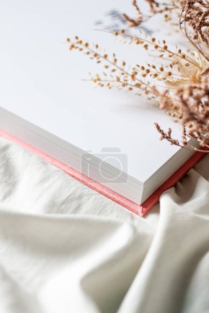 Téléchargez les photos : Livre ouvert avec des fleurs séchées sur drap de lit blanc - en image libre de droit