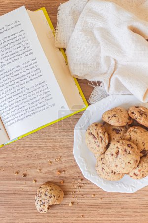 Photo for Top view of plate with pile of cookies with open book and linen fabric on wooden table - Royalty Free Image