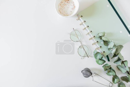 Téléchargez les photos : Planificateur, tasse de café et de lait, feuilles d'eucalyptus, verres, passoire à thé sur fond blanc. Pose plate, vue du dessus, espace de copie. - en image libre de droit