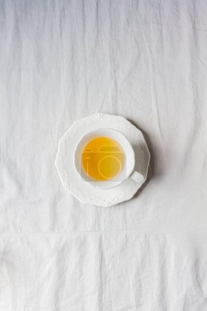 Téléchargez les photos : Tasse blanche de thé à la camomille, sur un fond en tissu blanc de coton. - en image libre de droit