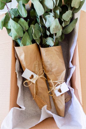 Téléchargez les photos : Bouquets d'eucalyptus vert dans une boîte artisanale. Concept de boutique de fleurs. - en image libre de droit