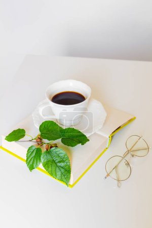 Foto de Taza de café negro, libro, vasos y hojas de mora sobre fondo blanco. Piso tendido, vista superior. Concepto primavera. - Imagen libre de derechos