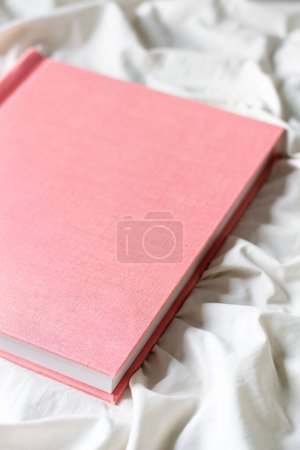 Téléchargez les photos : Vue rapprochée de l'album photo rose sur drap de lit blanc - en image libre de droit