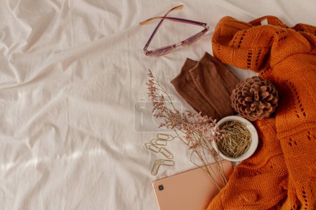 Photo for Autumn, fall composition. Beige linen bed with brown warm socks and sweater, golden paper clips, rose gold tablet, eucalyptus leaves, a cup of coffee and glasses. Lifestyle, fashion seasonal concept. - Royalty Free Image