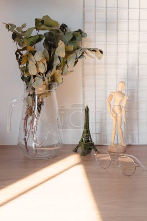 Foto de Ramas de eucalipto en un jarrón de vidrio con sombras de luz solar en el escritorio. Diseño romántico de decoración de interiores. - Imagen libre de derechos