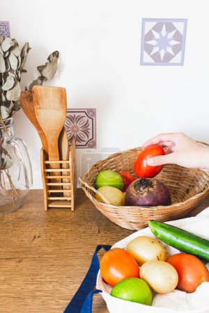 Photo for Female hand taking tomato from straw basket in the kitchen - Royalty Free Image