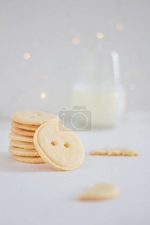 Téléchargez les photos : Biscuits vanila faits à la main en forme de bouton et verre de lait sur fond blanc. Couché plat, vue du dessus. - en image libre de droit