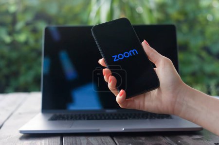 Photo for WROCLAW, POLAND - OCTOBER 2, 2023:Zoom logo, videotelephony software, displayed on iPhone screen with MacBook Pro in the background - Royalty Free Image