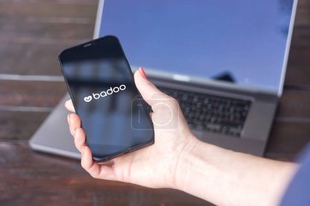 Photo for WROCLAW, POLAND - SEPTEMBER 14, 2023:Badoo logo, dating-focused social network founded by Russian entrepreneur Andrey Andreev, displayed on the iPhone held in hand with MacBook Pro in the background - Royalty Free Image