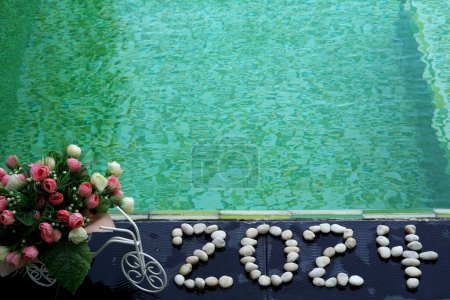 Photo for Year of the Dragon and Happy New Year 2024 written by stones on a floor tile background with artificial roses flowers close up green swimming pool - Royalty Free Image