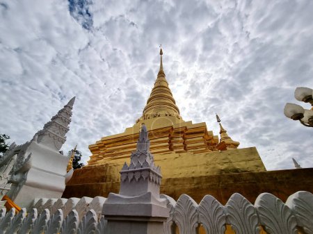 The perspective of a beautiful tall gold-colored chedi on clouds in the sky background of Wat Phra That Chae Haeng in Nan Province, Thailand.