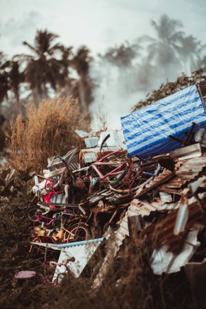 Photo for A vertical shot of an illegal garbage dump in the jungle; a scrap heap with rusty trash pieces and smashed bicycles in tropical settings with palms in the background, Thoddoo island, Maldives - Royalty Free Image