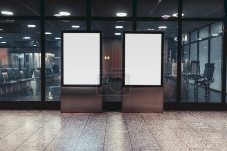 Téléchargez les photos : Un gabarit de deux bannières verticales blanches vierges à l'intérieur ; une maquette de deux panneaux d'affichage vides à l'intérieur d'un centre commercial ou d'un terminal d'aéroport en face du mur de verre en néon - en image libre de droit