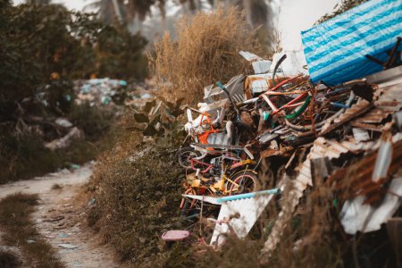 Foto de Un basurero ilegal ubicado junto a un camino de tierra; un vertedero con muchas hojas de metal oxidado, bicicletas viejas y otra basura - Imagen libre de derechos